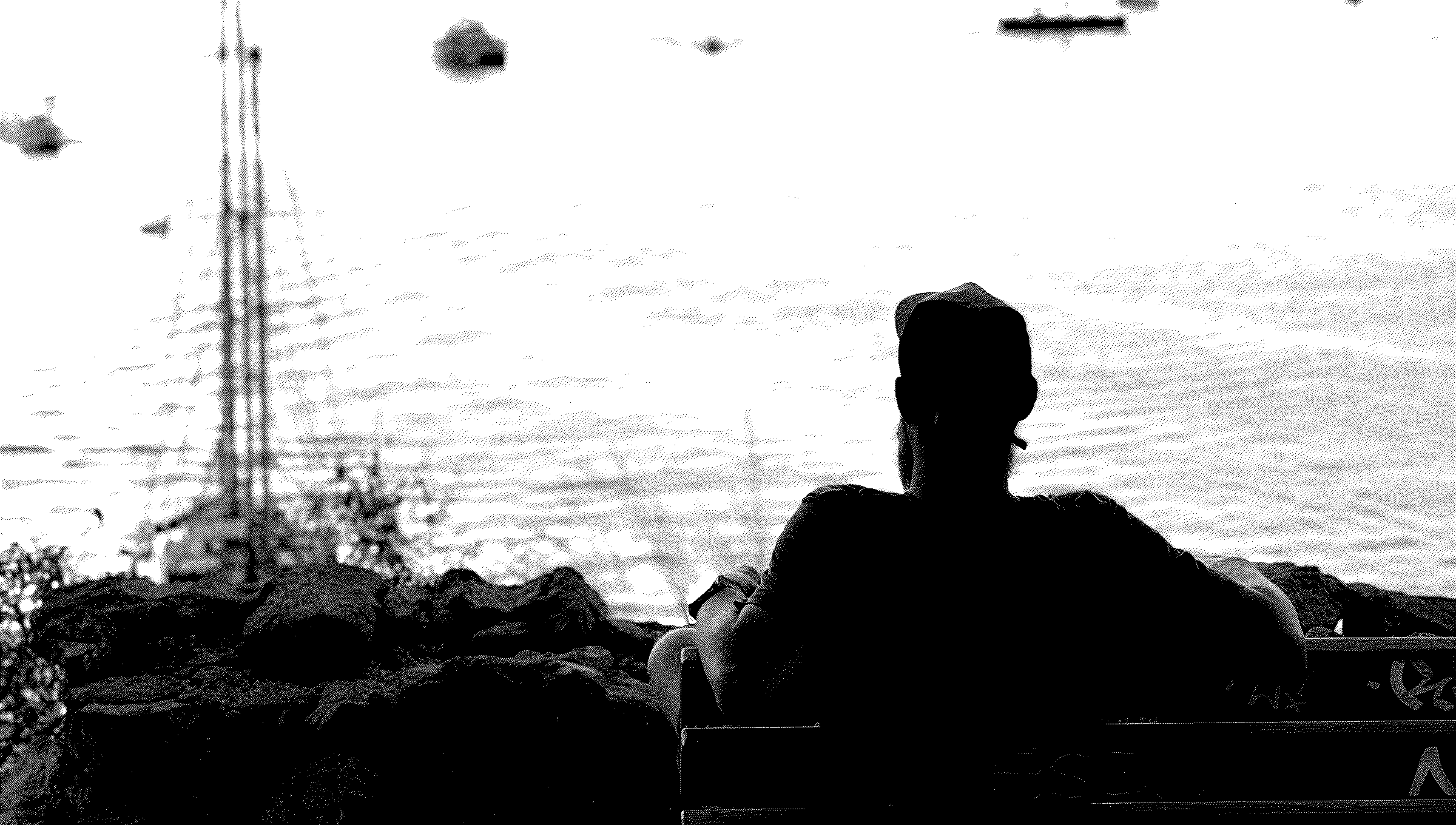 A person sitting on a bench, looking out over a bay full of moored boats at sunset.